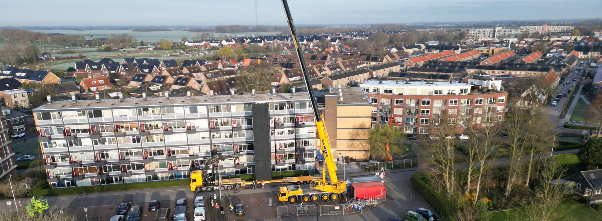 Crane getting ready to lift a prefabricated elevator from a truck in front of a residential building.